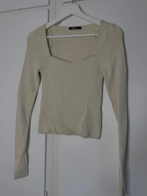 Ribbad beige långärmad topp - Trendig ribbad topp i beige med lång ärm och fyrkantig urringning. Sitter snyggt och har en figurnära passform som framhäver siluetten. Perfekt att styla med jeans eller kjol för en clean look.