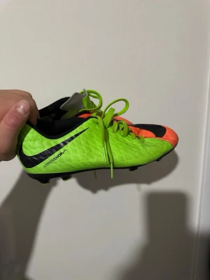 Nike Hypervenom grön/röd fotbollsskor - Säljer ett par Nike Hypervenom fotbollsskor i neon-grönt och orange med svarta detaljer. Skorna har snörning, låg profil och dobbar för spel på gräs. Perfekta för dig som vill sticka ut på planen och få bra grepp i spelet.