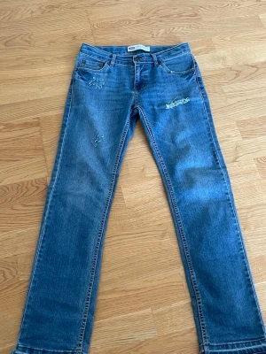 Levi's 511 Slim blå jeans - Säljer ett par klassiska blå Levi's 511 Slim jeans med raka ben och slitningar på låret och knät. Jeansen har fem fickor, knappgylf och är tillverkade i denim. Perfekta för en avslappnad och trendig look.