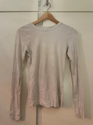 Vit långärmad topp från H&M - En enkel och stilren vit långärmad topp från H&M. Toppen har rund halsringning och är tillverkad i mjuk bomull som känns skön mot huden. Perfekt att matcha med jeans eller kjol för en clean look.