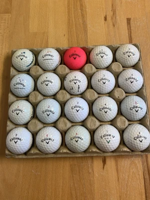 20 Callaway golfbollar i kartong - Säljer ett set med 20 golfbollar från Callaway, mestadels vita men en är röd. Bollarna ligger i en praktisk kartong och har klassisk rund form med dimple-mönster. Perfekt för dig som vill fylla på golfväskan inför nästa säsong.