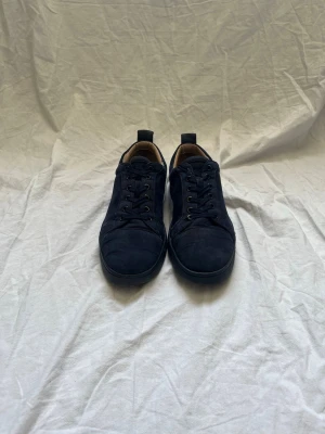 Mörkblåa låga sneakers i mocka - Snygga mörkblå sneakers i mocka med klassisk låg profil och rund tå. Skorna har svarta snören, diskreta sömmar och dragflikar bak. Insidan är fodrad i beige textil för extra komfort. Perfekta för en clean och stilren look.