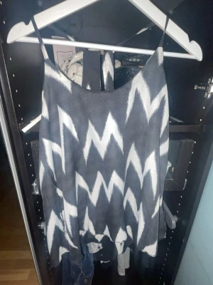 Svartvit linnetopp med zigzag-mönster - Säljer en snygg linnetopp från Lille Rose med svart och vitt zigzag-mönster. Toppen har tunna axelband och en öppen rygg med racerback-design. Perfekt för dig som gillar unika mönster och vill sticka ut lite extra.