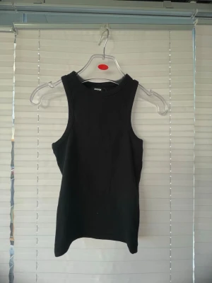 Svart ribbad tanktop från BikBok - Säljer en svart ribbad tanktop från BikBok. Modellen är ärmlös med rund halsringning och tight passform. Perfekt att styla till jeans eller kjol för en clean och enkel look.