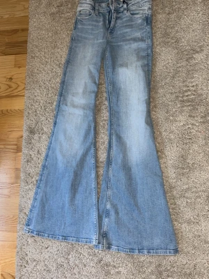 Ljusblå Gina jeans. Helt nya - Säljer ett par ljusblå jeans med hög midja och rejält utsvängda ben. Klassisk femficksmodell med dragkedja och knapp framtill. Jeansen har en snygg tvättad look och är perfekta för dig som gillar retrostil.