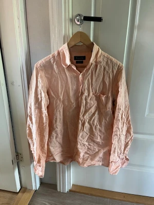 Orange linneskjorta - Säljer en orange skjorta i linne med klassisk krage och bröstficka. Skjortan har långa ärmar och knäppning framtill. Perfekt för en avslappnad och stilren look.