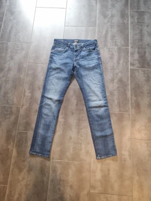 Blåa jack&Jones byxor - Ett par klassiska blå jeans från jack&Jones  med raka ben och lätt slitna detaljer på framsidan. Jeansen har fem fickor och normal midja. Tillverkade i denim med en snygg tvättad look som ger en avslappnad vibe. Byxorna är i storlek w31 och L32