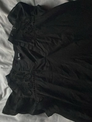 Svart blus med spets från Vero Moda - Snygg svart blus från Vero Moda med korta ärmar och dekorativ spets upptill. Blusen har en avslappnad passform och är tillverkad i ett mjukt bomullsmaterial. Perfekt för dig som gillar stilrena detaljer och enkel design. Köpt i Tyskland 
