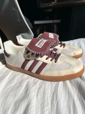 Adidas Samba Wales Bonner ponyhair cream  - Säljer ett par Adidas Samba OG sneakers i bordeaux och vitt med klassiska tre ränder på sidan. Skorna har en gummisula, mockadetaljer och bred plös med Adidas-logga. Perfekta för dig som gillar retrostil och vill sticka ut med snygga färgkombos.