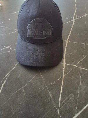 Svart keps med broderad logga - Snygg svart keps med böjd skärm och broderad logga framtill där det står 'Beyling'. Tillverkad i ett slitstarkt material och har en klassisk passform. Perfekt för att komplettera din streetwear-look.