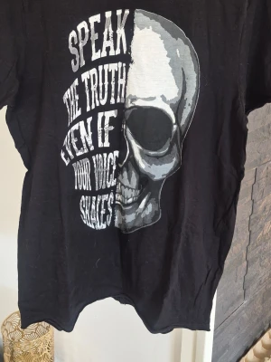 Svart t-shirt med dödskalletryck - Cool svart t-shirt med stort tryck av en dödskalle och texten 'Speak the truth even if your voice shakes' i vitt. T-shirten har rund hals och korta ärmar, perfekt för dig som gillar edgy och statement-plagg.