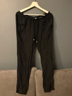 Svarta mjukisbyxor från Divided - Svarta mjukisbyxor från Divided med elastisk midja och dragsnöre. Byxorna har raka ben och ribbade muddar vid benslut. 