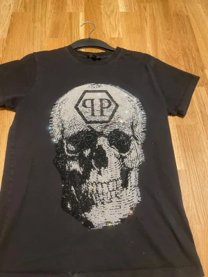 Svart t-shirt med döskalle Philipp Plein - Säljer en svart t-shirt från Philipp Plein i storlek S. T-shirten har ett stort döskallemotiv framtill i glittriga paljetter och en klassisk rund hals. Perfekt för dig som vill sticka ut med en edgy och unik stil.