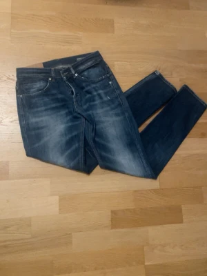 Blå dondup skinny fit jeans med slitningar - Snygga blå jeans i slim fit-modell med tydliga slitningar och tvättade detaljer. Klassisk femficksdesign och orange sömmar. Jeansen har en modern look och passar perfekt till en avslappnad stil.