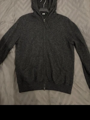 Mörkgrå hoodie från Gobi - Säljer en mörkgrå hoodie från Gobi i mjuk mongolisk kashmir. Hoodien har dragkedja framtill, två fickor och ribbade muddar. Perfekt för dig som vill ha något riktigt bekvämt och stilrent med huva. Används inför höst, vår och vinter! Perfekt för kylan!