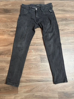 Svarta slim fit jeans från Replay - Säljer ett par svarta slim fit jeans från Replay med klassisk femficksmodell och dragkedja. Jeansen har en diskret tvättad look och raka ben. Perfekta för dig som gillar en stilren och modern vibe.