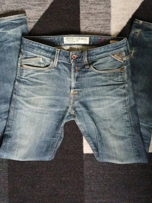 Blåa jeans från Replay - Snygga blåa jeans från Replay med klassisk femficksmodell och slitna detaljer. Jeansen har raka ben och ljus tvätt med kontrastsömmar. Perfekta för en avslappnad och trendig stil.