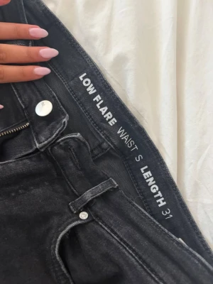 Svarta low flare jeans, längd 31 - Säljer ett par svarta low flare jeans med midja i storlek S och längd 31. Jeansen har klassisk femficksdesign, dragkedja och knapp framtill samt utsvängda ben. Perfekta för dig som gillar en trendig och avslappnad look.
