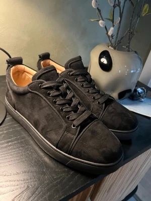 Svarta sneakers i mocka - Snygga svarta sneakers i mocka med klassisk låg profil och svarta skosnören. Insidan är beige och har guldfärgad logga. Perfekta för dig som gillar stilrena och exklusiva skor med en lyxig känsla. Tvärfeta skor som knappt är använda då de va för stora. Du vet varför de är så billiga 🤗