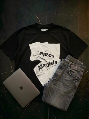 Maison Margiela svart t-shirt med vitt tryck - Säljer en svart t-shirt från Maison Margiela med ett stort vitt grafiskt tryck framtill. T-shirten har rund hals och korta ärmar. Perfekt för dig som gillar statement-plagg och vill sticka ut med en unik design. Helt oanvänd och är en perfekt stilren T-shirt till skolstarten. Tröjan är märkt med storlek 48 men passar till storlek L.