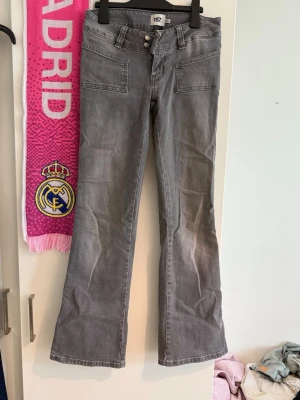 Grå bootcut jeans från 157 - Snygga grå jeans från 157 med bootcut-modell och dubbla knappar i midjan. Jeansen har stora framfickor och är tillverkade i ett klassiskt denimtyg. Perfekta för en trendig och avslappnad stil.