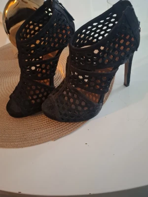 Svarta nätmönstrade high heel pumps - Säljer ett par svarta pumps med höga klackar och coolt nätmönster. Skorna har öppen tå och dragkedja bak för enkel påtagning. Materialet ser ut att vara mockaimitation och designen är riktigt trendig. Finns inte i butik längre (äldre modell) pris kan diskuteras!