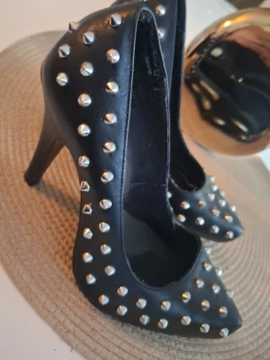 Svarta pumps med nitar från Din Sko - Säljer ett par svarta pumps från Din Sko med spetsig tå och höga klackar. Skorna är täckta med silvriga nitar för en edgy look. Materialet är konstläder och de har en klassisk pumpsform som passar till många olika stilar. Dessa skor säljs inte längre vad jag förstod :)