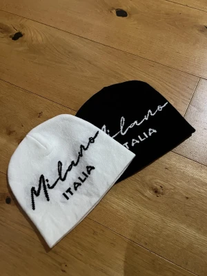 Milano Italia svart och vit mössa - Två stilrena mössor från Milano Italia, en i svart och en i vitt. Båda har broderad text i kontrasterande färg framtill. Klassisk, mjuk och stretchig modell som passar perfekt till streetwear eller casual outfits .Båda för 100 och en för 50.
