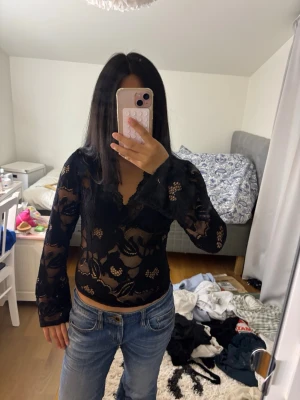 Svart spetsblus med v-ringning - Säljer en svart, transparent spetsblus med v-ringning och långa ärmar. Blusen har ett blommigt spetsmönster och sitter tight mot kroppen. Perfekt för dig som vill ha en trendig och elegant topp med snygga detaljer.