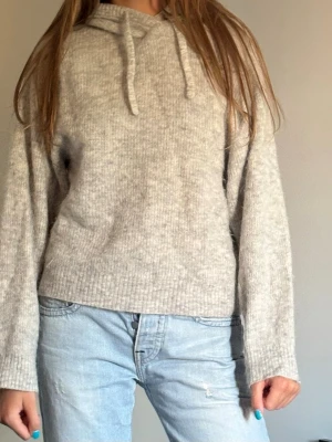 Ljusgrå stickad hoodie - En mysig ljusgrå stickad hoodie med huva från & other stories. 😊Säljer då den inte kommer till användning. Tröjan har en avslappnad passform. Den är inte helt nyskick, kan vara lite nopprig men inga andra defekter!