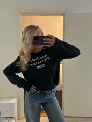 Svart långärmad tröja Acne Studios - Svart långärmad tröja Acne Studios med vit text 'Acne Studios STOCKHOLM 1996' på bröstet. Tröjan har avslappnad passform och rund halsringning. Perfekt till jeans eller kjol för en cool och enkel stil. Obs ej äkta 