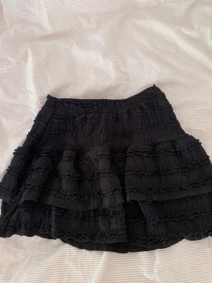 Svart volangkjol  - Säljer en svart volangkjol i ganska tjockt material med detaljer i tyget. Aldrig använd💖