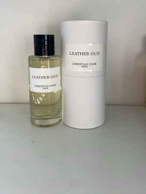 Leather Oud parfym från Dior 125 ml - Leather Oud från Christian Dior är en exklusiv parfym i en stilren, genomskinlig glasflaska med svart lock. Doften har tydliga inslag av läder och oud, vilket ger en djup och lyxig känsla. Flaskan har en minimalistisk design med vit etikett och svart text. EJ ANVÄND, BOX INGÅR
