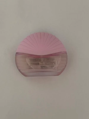 Parfymflaska i rosa snäckform - Säljer en unik parfymflaska i snäckformad design med mjuka rosa och transparenta toner. Flaskan har en räfflad ovandel och är tillverkad i glas och plast. Perfekt som en söt detalj på sminkbordet eller i väskan.