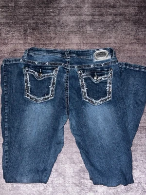 Y2k flare jeans med blingade bakfickor - Säljer ett par blå flarejeans med diamant/paljetter detaljer på bakfickorna och framfickorna. Jeansen är knappt använda och i fint skick förutom de två bältes-flärparna som åkt upp lite som visas på bild (går att lösa med enstaka stygn och syns inte när de används) och är perfekta för dig som gillar statement-plagg. Stlk M men stretchiga så kan passa L.   Pris kan diskuteras vid snabb affär