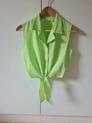 Dam topp, str M - Limegrön ärmlös topp/skjorta med knytning framtill. Det saknas info om material, met det känns som viskos eller lyocell