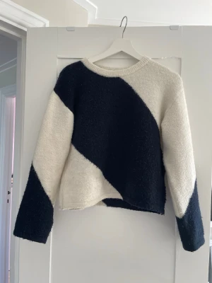 Svartvit stickad tröja med diagonal design - Säljer en snygg stickad tröja i svart och vitt med diagonal färgblock-design. Tröjan har rund halsringning och långa ärmar. Perfekt för dig som gillar en modern och stilren look.