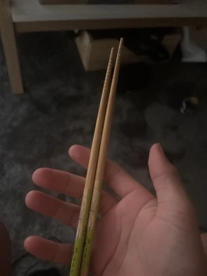 Träpinnar med grönt mönster - Säljer ett par ätpinnar i trä med grönt och vitt mönster längst ner. Perfekta till sushi eller nudlar och har räfflad topp för bättre grepp. Snygg detalj till köket eller som present.