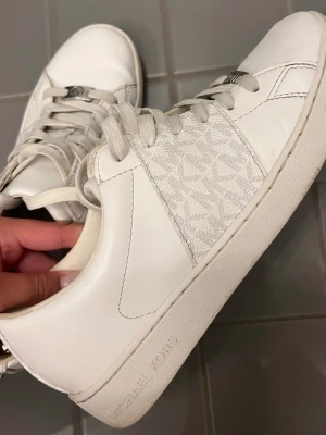 Vita sneakers från Michael Kors - Vita sneakers från Michael Kors, med extra detaljer. Knappast använda, i storlek 38. Köpta för 1600kr och säljer för 960kr❤️
