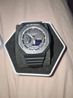 Svart Casio G-Shock klocka - Säljer en svart Casio G-Shock klocka med robust design och digitalt/analogt urverk. Klockan har en rund urtavla med silver- och grådetaljer samt skyddande boett. Armbandet är i slitstark syntet och klockan har Carbon Core Guard för extra hållbarhet.