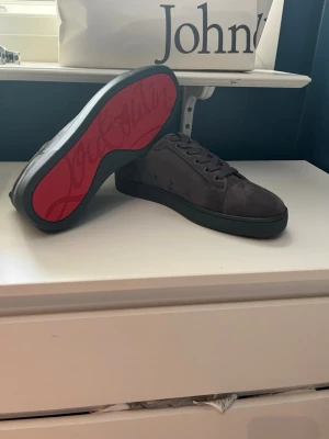 Christian Louboutin helt nya  - Helt nya och oanvända. Storlek 43. Säljer pga köpte fel storlek. Snygga grå sneakers i mocka med klassisk låg profil och ikonisk röd sula. 