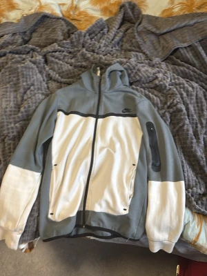 Nike hoodie i grått och vitt - Nike hoodie med dragkedja i grått och vitt. Stora vita partier framtill och på ärmarna, svarta detaljer och Nike-logga på bröstet. Huva och fickor med dragkedja. Perfekt för en chill och sportig look.