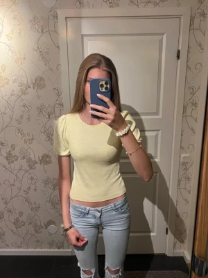 Ljusgul ribbad topp med puffärm - Säljer en ljusgul ribbad topp med puffärmar och rund hals. Toppen är croppad och har en slim passform som sitter snyggt på kroppen. Perfekt till jeans eller kjol för en fräsch look. Skulle säga att den är som storlek xs. Inte använd så mycket så är i bra skick.