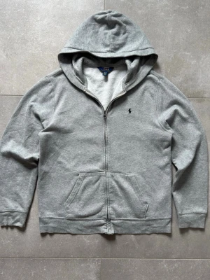 Ralph Lauren ziphoodie - Klassisk grå ziphoodie från Polo Ralph Lauren med broderad marinblå logga på bröstet. Stilren modell och ett tidlöst plagg som passar till det mesta. 📏Storlek: XL i barnstorlek vilket är som S/M i vanlig 🎨Färg: Grå 🏷️Märke: Polo Ralph Lauren ✨Skick: Mycket bra skick, lite nopprig Skick gärna ett meddelande vid frågor eller om du vill ha fler bilder. 