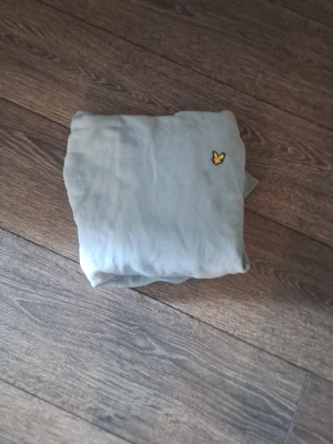 Två lylen scott tröjor med logga - Säljer två lyken scott tröjor i olika färger 100 kr st 200 för båda, en ljusgrå och en mörkbrun, båda med en liten gul broderad logga på bröstet. Tröjorna har en enkel och stilren design, perfekta för en avslappnad look. Materialet känns mjukt och bekvämt.