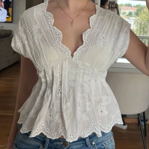 Vit blus - Söt vit blus med broderade blommor och romantisk spetskant längs den djupa v-ringningen. Den har korta ärmar, smock i ryggen och vågig nederkant. Från Gina Tricot i storlek xs🤍