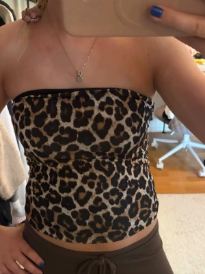 Leopardmönstrad tubtopp - Säljer en snygg tubtopp med leopardmönster i bruna och svarta toner. Toppen är axelbandslös och har en tight passform som sitter på plats. Perfekt för dig som vill sticka ut lite extra med ett djuriskt print. FINNS två små blåa fläckar jag ej fått bort tyvärr men de är väldigt små och syns knappast! Skriv pm vid funderingar!☺️