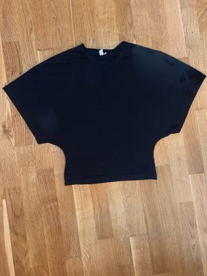 Svart croppad topp med vida ärmar - Säljer en svart croppad topp med vida, korta ärmar och rund hals. Toppen har en tight midja och är tillverkad i mjukt material, perfekt för en avslappnad och trendig look.