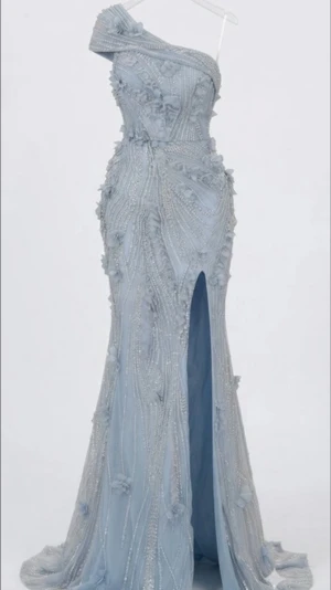 Ljusblå axelbandslös balklänning - Elegant ljusblå klänning med asymmetrisk axel, dekorerad med pärlor och 3D-blommor. Figurnära passform och hög slits framtill ger en lyxig känsla. Materialet är glansigt och skimrande, perfekt för speciella tillfällen.