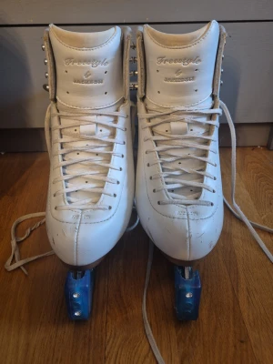 Jackson Freestyle 2190 – storlek 5W - Säljer ett par klassiska vita konståkningsskridskor från Jackson med högt skaft, snörning och blåa skydd på skenorna. Skridskorna har robust läderyta och träklack, perfekta för träning på isen. Snygg och tidlös modell för dig som gillar konståkning. Funkar bra för dig som är i de högre nivåerna på nybörjar konståkningen eller om du nyligen blivit tävlingsåkare. Storleken är ungefär som skostorleken 36. Skenan kan behöva slipas